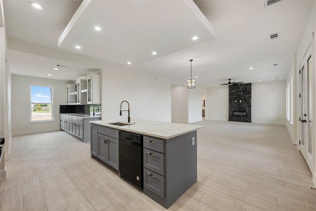 kitchen with a center island with sink, sink, black dishwasher, gray cabinetry, and light stone counters