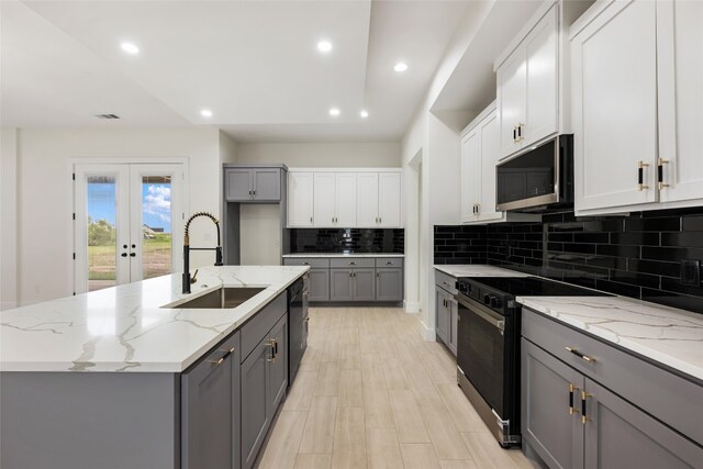 kitchen with light stone countertops, black appliances, sink, a kitchen island with sink, and gray cabinetry