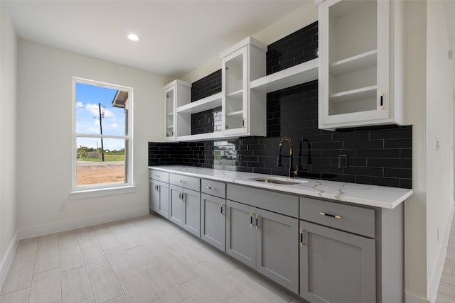 kitchen with light stone countertops, sink, gray cabinetry, and tasteful backsplash