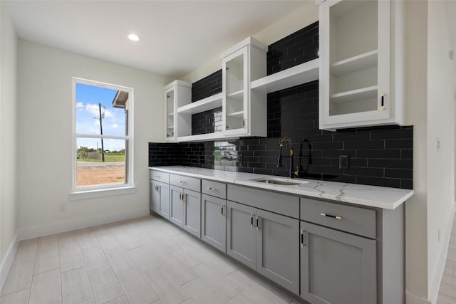 kitchen featuring open shelves, baseboards, gray cabinets, and a sink