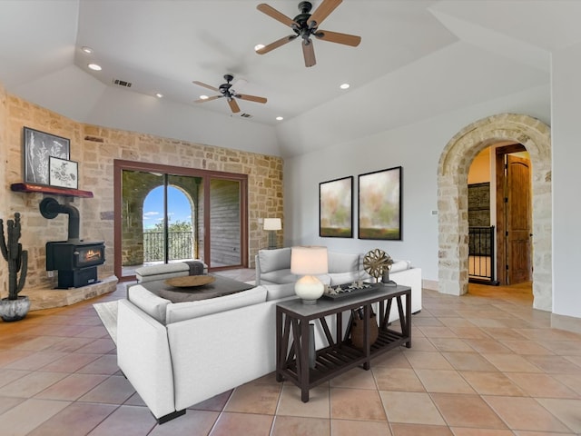 living room with a wood stove, ceiling fan, lofted ceiling, and light tile patterned flooring