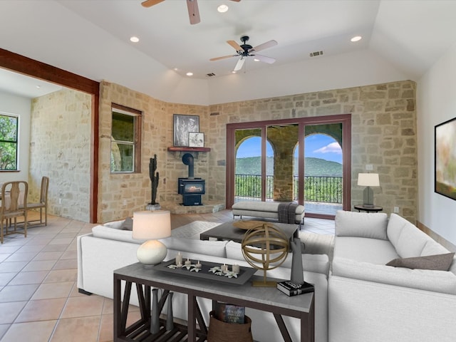 tiled living room with lofted ceiling, ceiling fan, a wealth of natural light, and a wood stove