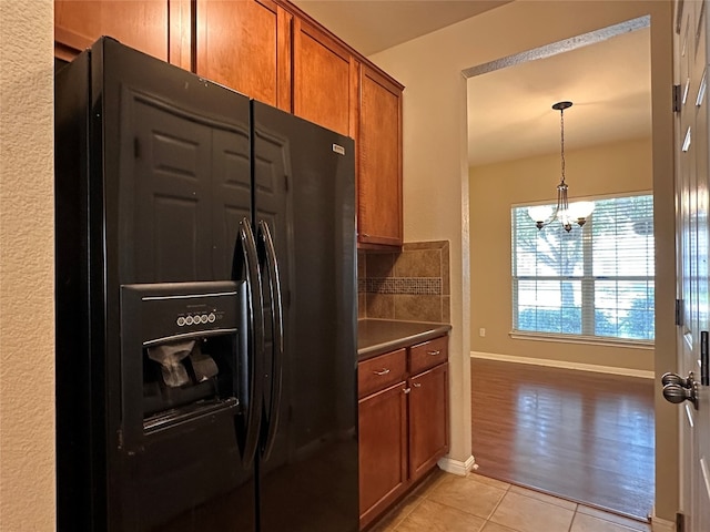 kitchen with black refrigerator with ice dispenser, pendant lighting, a notable chandelier, and light wood-type flooring