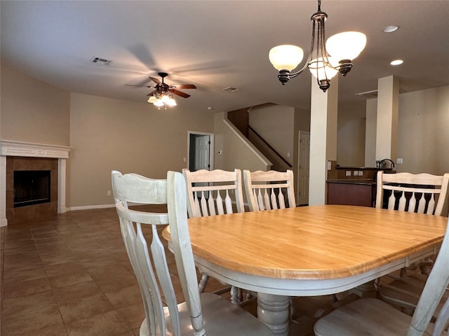 dining space with dark tile patterned flooring, ceiling fan with notable chandelier, and a tile fireplace