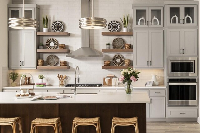 kitchen with wall chimney exhaust hood, a kitchen breakfast bar, appliances with stainless steel finishes, and light hardwood / wood-style flooring