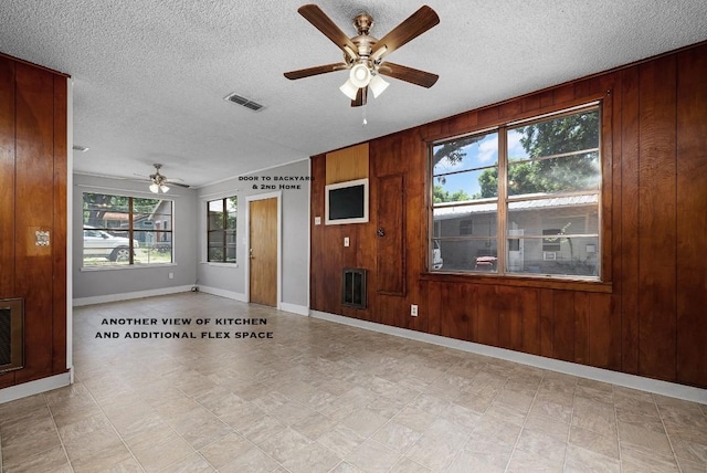 interior space featuring ceiling fan, wooden walls, and a textured ceiling