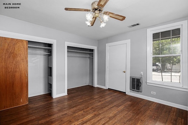 unfurnished bedroom featuring dark wood-type flooring, ceiling fan, two closets, and heating unit