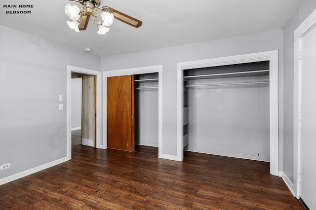 unfurnished bedroom featuring multiple closets, dark wood-type flooring, and ceiling fan