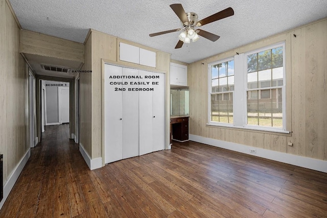 unfurnished bedroom featuring a textured ceiling, ceiling fan, wood walls, and dark hardwood / wood-style flooring