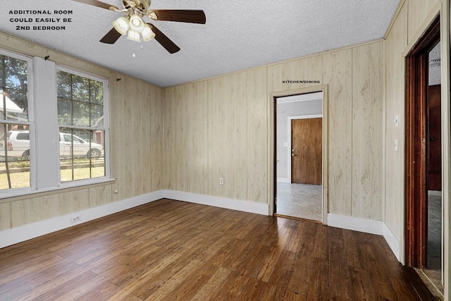 empty room featuring a textured ceiling, ceiling fan, wood-type flooring, and wooden walls