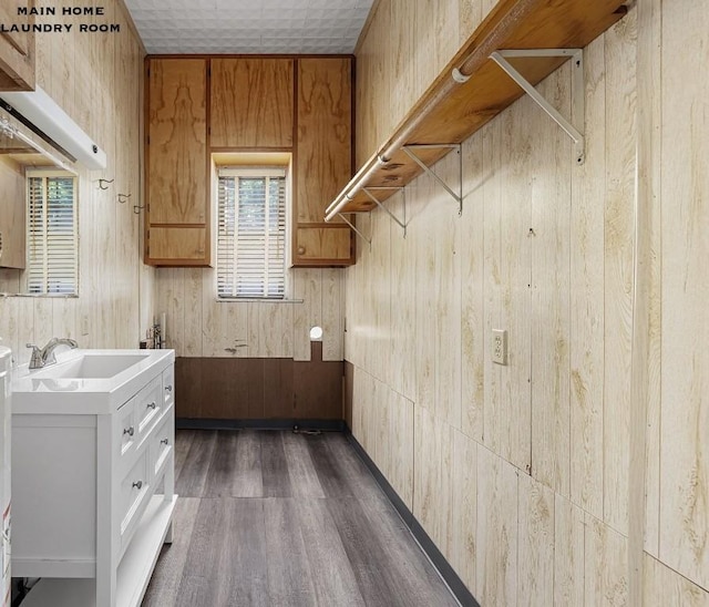 kitchen with dark wood-type flooring, white cabinets, wood walls, and sink