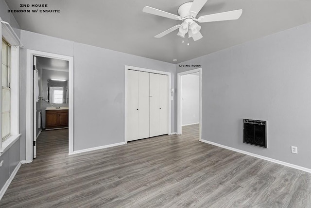 unfurnished bedroom featuring hardwood / wood-style floors, multiple windows, heating unit, ceiling fan, and a closet