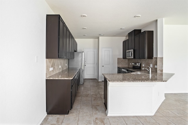 kitchen featuring light stone counters, stainless steel appliances, kitchen peninsula, and decorative backsplash