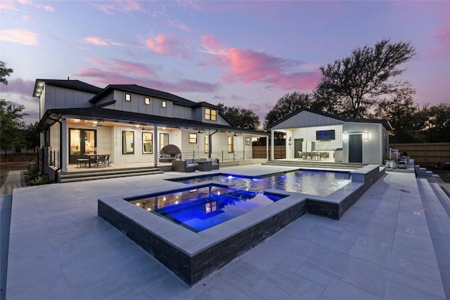 pool at dusk with a patio area and an in ground hot tub