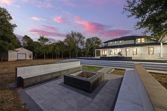 patio terrace at dusk with a garage, an outdoor structure, and an outdoor fire pit