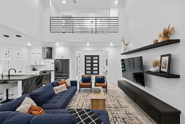 living room with a towering ceiling, sink, and light hardwood / wood-style floors