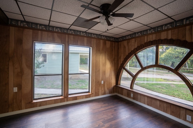 empty room with a paneled ceiling, ceiling fan, plenty of natural light, and dark hardwood / wood-style floors