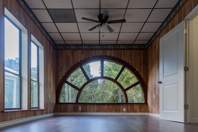 interior space featuring hardwood / wood-style floors, ceiling fan, wood walls, and a drop ceiling