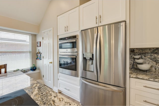 kitchen featuring vaulted ceiling, light stone counters, stainless steel appliances, and white cabinets