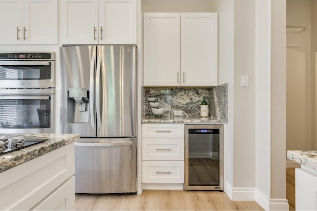 kitchen with beverage cooler, appliances with stainless steel finishes, light hardwood / wood-style floors, light stone counters, and white cabinets