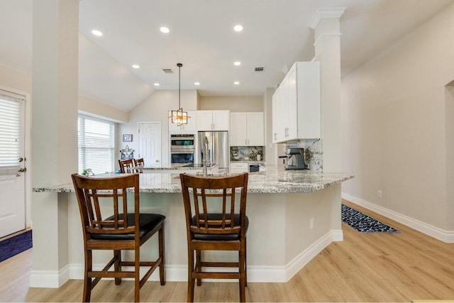 kitchen with vaulted ceiling, decorative light fixtures, light hardwood / wood-style flooring, appliances with stainless steel finishes, and white cabinets