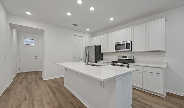 kitchen with white cabinetry, sink, stainless steel appliances, light hardwood / wood-style flooring, and an island with sink