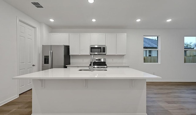 kitchen with white cabinets, stainless steel appliances, light hardwood / wood-style flooring, and a kitchen island with sink