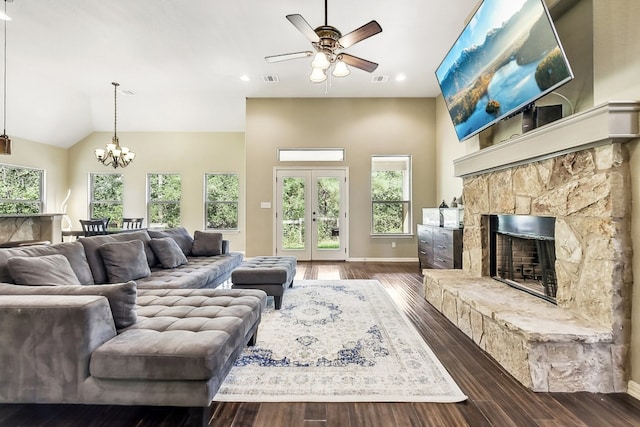 living room featuring dark hardwood / wood-style floors, ceiling fan with notable chandelier, a stone fireplace, french doors, and lofted ceiling