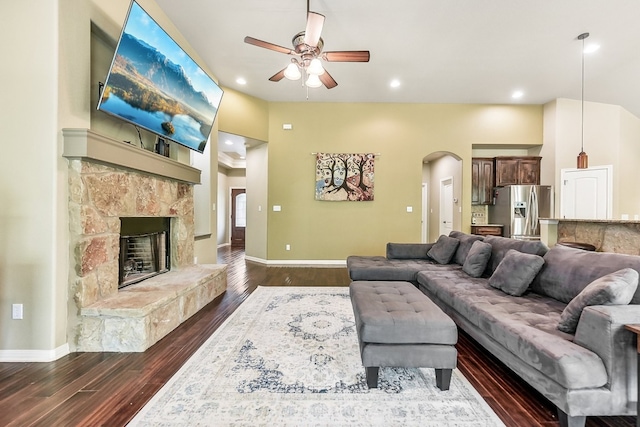 living room with dark wood-type flooring, ceiling fan, and a stone fireplace