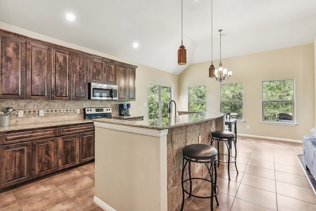 kitchen with an island with sink, vaulted ceiling, a notable chandelier, and light stone counters