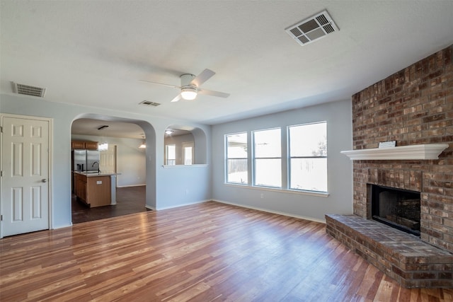 unfurnished living room featuring ceiling fan, dark hardwood / wood-style flooring, a textured ceiling, and a brick fireplace