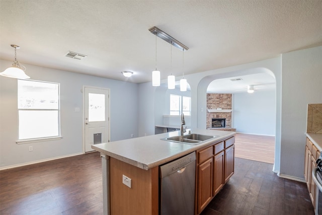 kitchen featuring a large fireplace, stainless steel appliances, decorative light fixtures, an island with sink, and sink