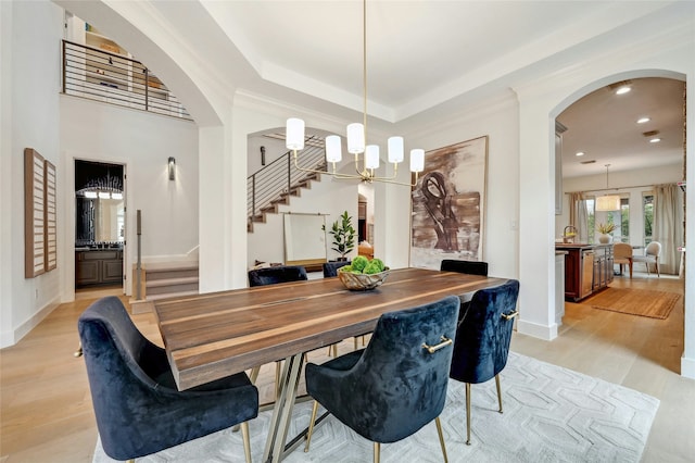 dining space with a notable chandelier, crown molding, sink, a raised ceiling, and light hardwood / wood-style flooring