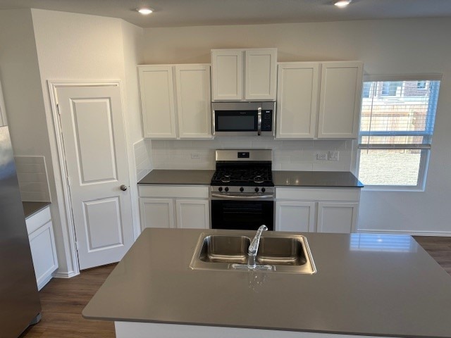 kitchen with sink, stainless steel appliances, an island with sink, white cabinets, and dark hardwood / wood-style flooring