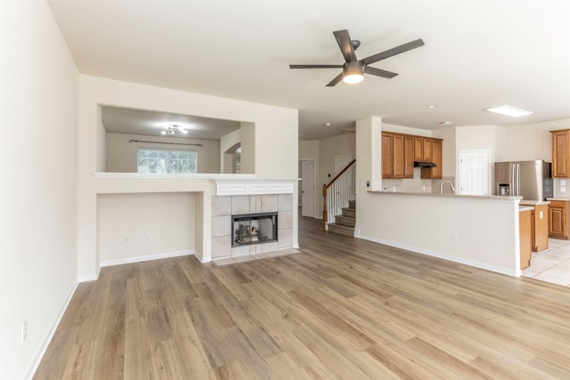 unfurnished living room with ceiling fan, light wood-type flooring, a tiled fireplace, and sink