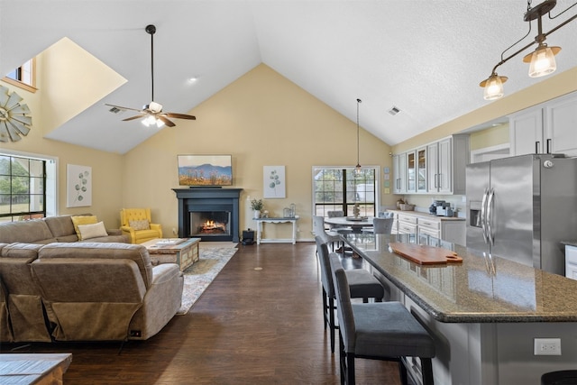 kitchen with white cabinets, dark hardwood / wood-style floors, dark stone counters, ceiling fan, and stainless steel fridge with ice dispenser