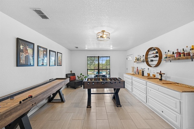 game room with bar area, an inviting chandelier, and a textured ceiling