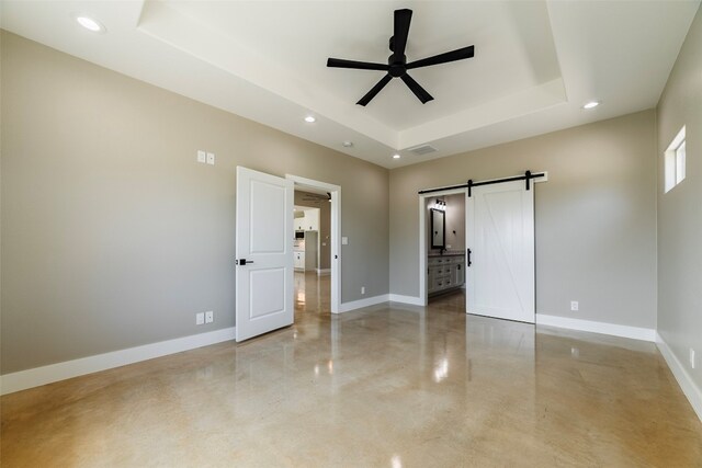 unfurnished bedroom featuring ceiling fan, a tray ceiling, and a barn door