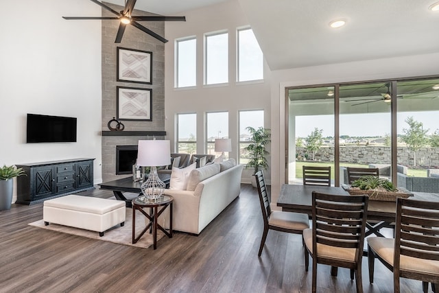 living room with dark hardwood / wood-style floors, ceiling fan, high vaulted ceiling, and a tiled fireplace