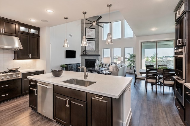 kitchen featuring a large fireplace, a kitchen island with sink, sink, pendant lighting, and range hood