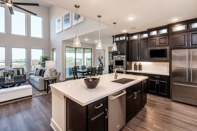 kitchen featuring built in appliances, dark hardwood / wood-style floors, a healthy amount of sunlight, and an island with sink