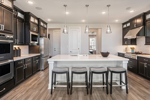 kitchen with stainless steel appliances, pendant lighting, wood-type flooring, a breakfast bar area, and a center island with sink