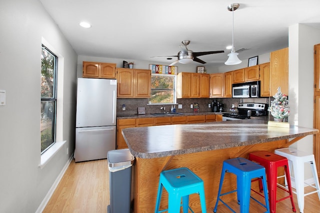 kitchen with appliances with stainless steel finishes, a breakfast bar, sink, ceiling fan, and light wood-type flooring