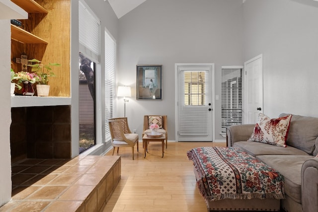 living room with light hardwood / wood-style flooring, a tiled fireplace, and high vaulted ceiling