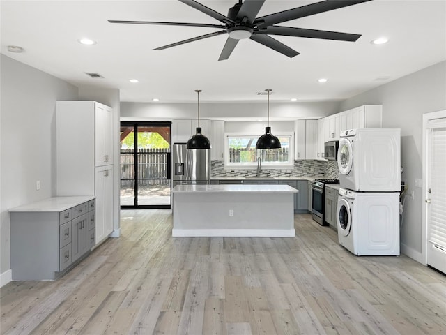 kitchen featuring stacked washing maching and dryer, light hardwood / wood-style flooring, stainless steel appliances, and ceiling fan