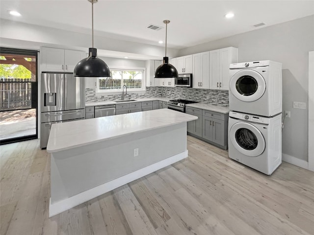 kitchen with light wood-type flooring, appliances with stainless steel finishes, decorative light fixtures, and stacked washing maching and dryer