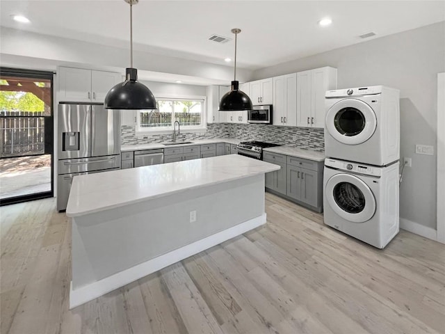9614 Newfoundland Cir, Austin, TX 78758 - kitchen featuring stainless steel appliances, stacked washer / dryer, gray cabinets, tasteful backsplash, and a center island
