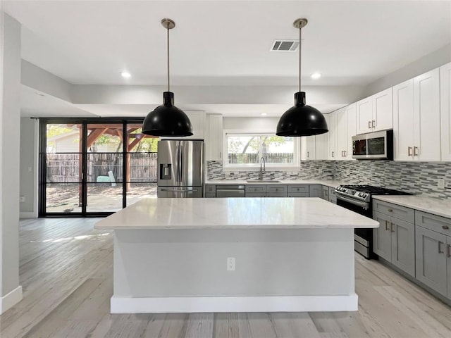 9614 Newfoundland Cir, Austin, TX 78758 - kitchen featuring appliances with stainless steel finishes, gray cabinets, a kitchen island, tasteful backsplash, and recessed lighting
