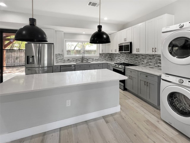 kitchen featuring white cabinets, light hardwood / wood-style flooring, stainless steel appliances, sink, and stacked washer / dryer