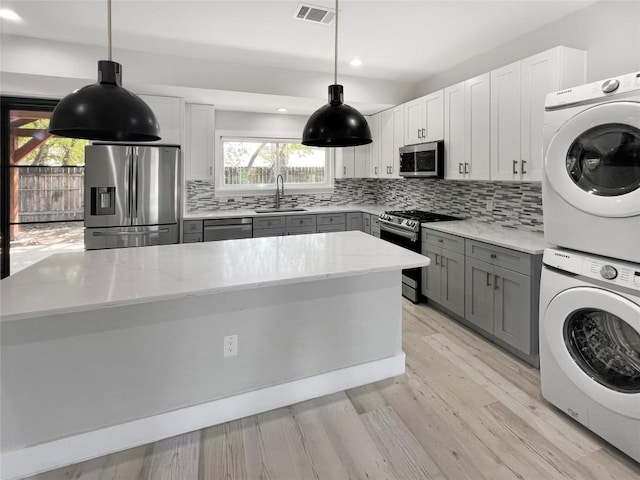 9614 Newfoundland Cir, Austin, TX 78758 - kitchen with appliances with stainless steel finishes, stacked washer / dryer, gray cabinetry, backsplash, and light stone counters